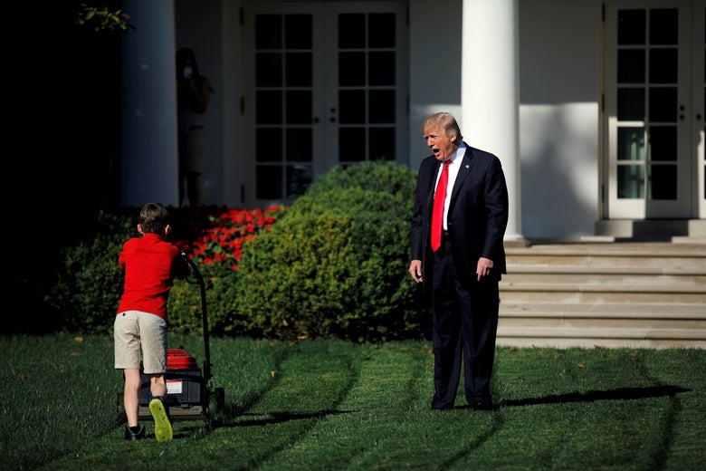 Trump, with his hands at his sides, speaks toward a small boy in a red shirt who is mowing the White House lawn.